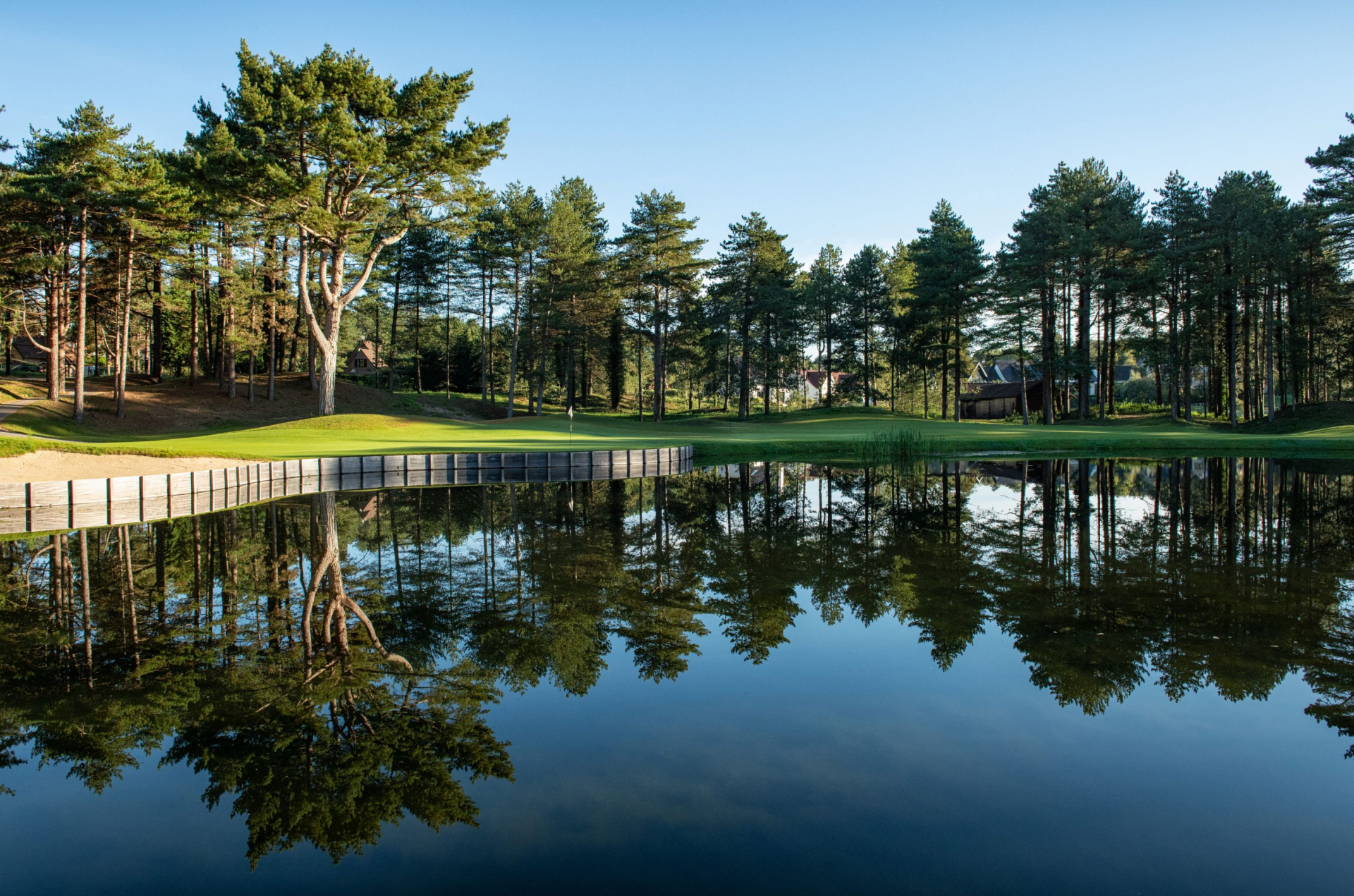Große Wasserfläche auf einem Golfplatz, in der sich umliegende grüne Bäume spiegeln
