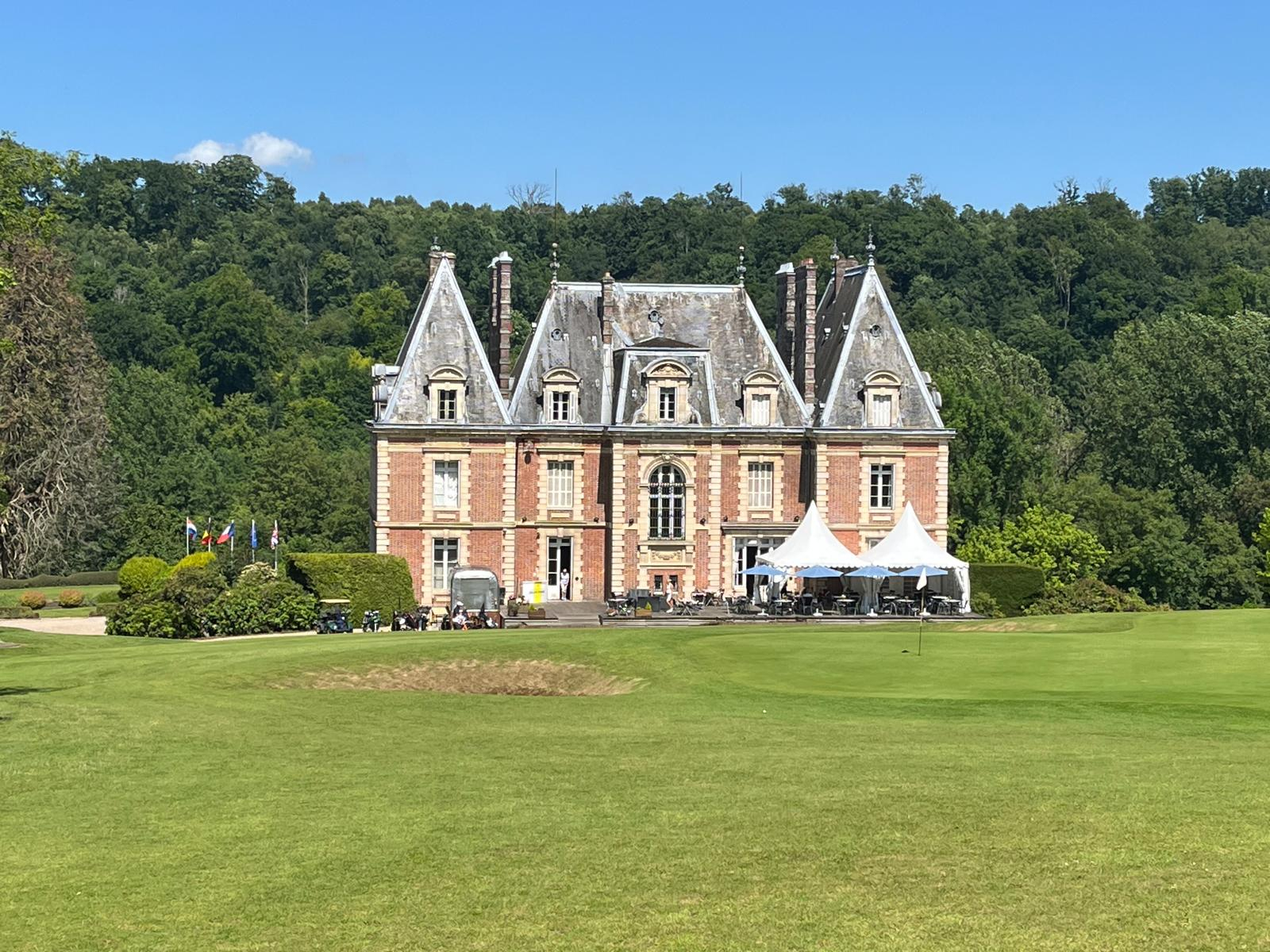 Schloss mit einem Golfplatz im Vordergrund und dichten grünen Bäumen im Hintergrund