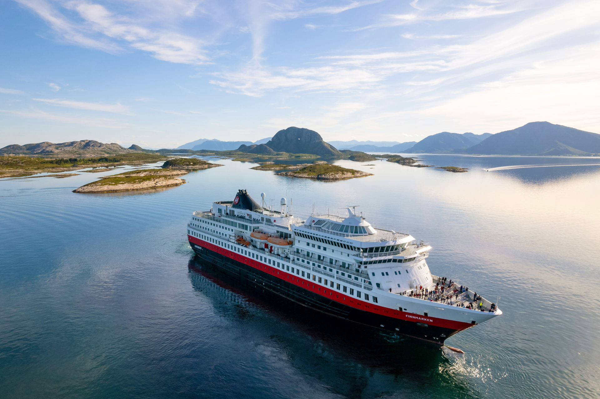 Die MS Finnmarken fährt durch eine norwegische Schärenlandschaft, im Hintergrund Berge.                                 - © Hurtigruten | Michel Afflerbach                                                            