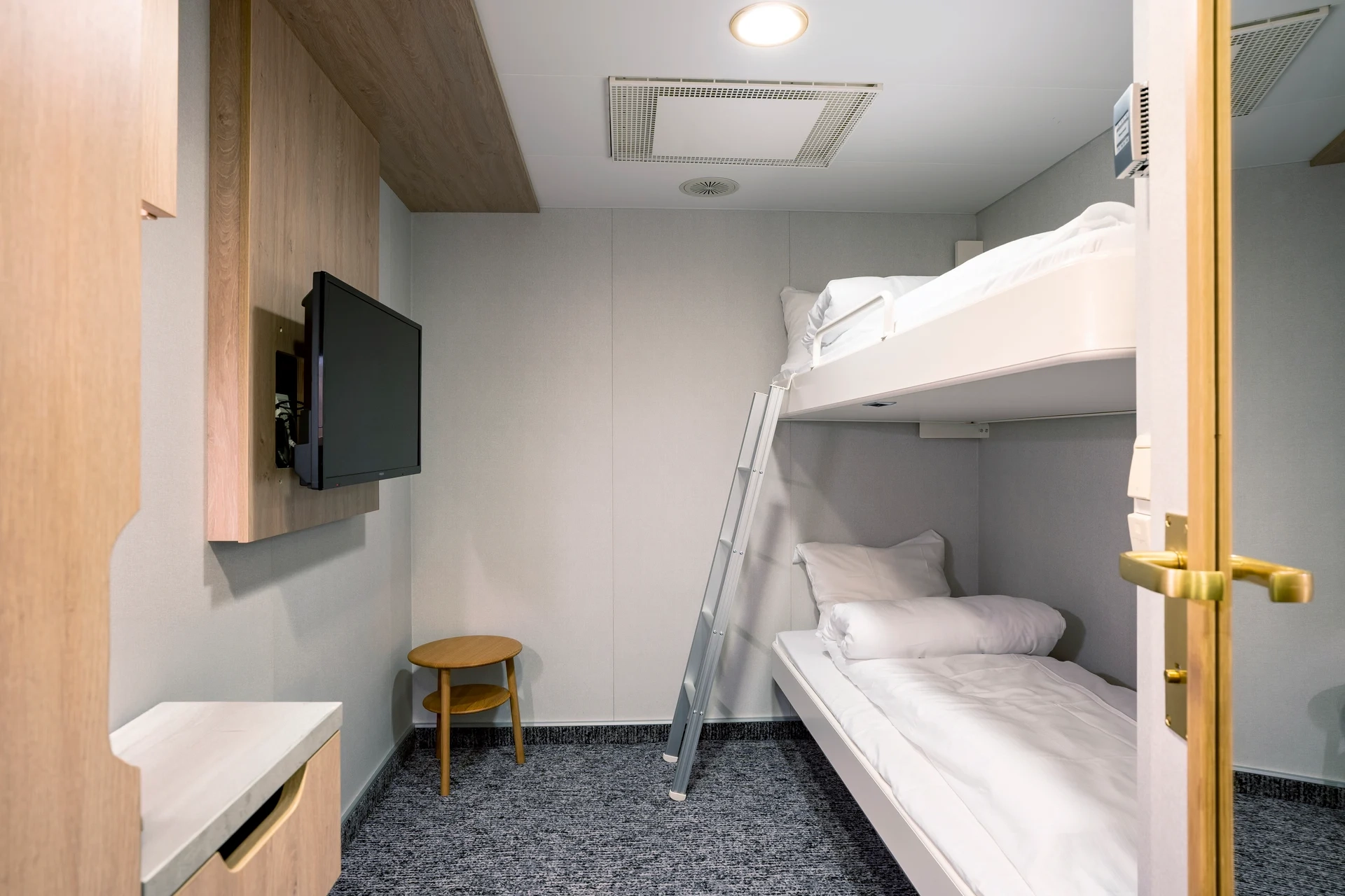 Eine kompakte Innenkabine an Bord der MS Finnmarken mit Etagenbett, Leiter, Flachbild-TV und kleinem Holzhocker.                                 - © Hurtigruten | Andrea Klaussner                                                            